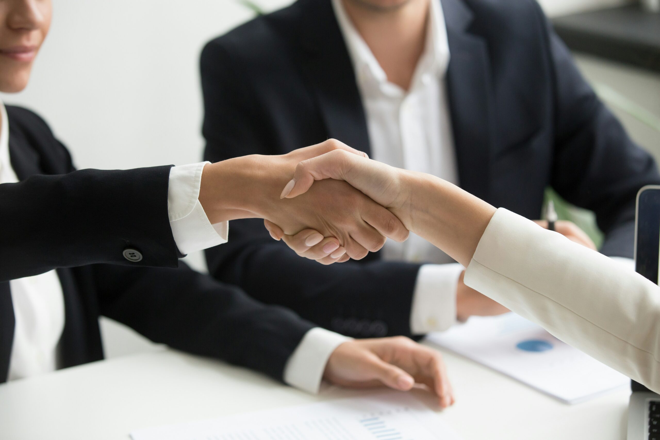 Two professionals shaking hands during a sales meeting, adapting communication style to the buyer